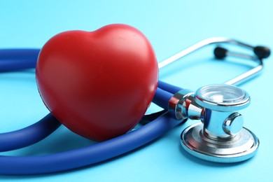 Photo of Cardiology. Stethoscope and red decorative heart on light blue background, closeup