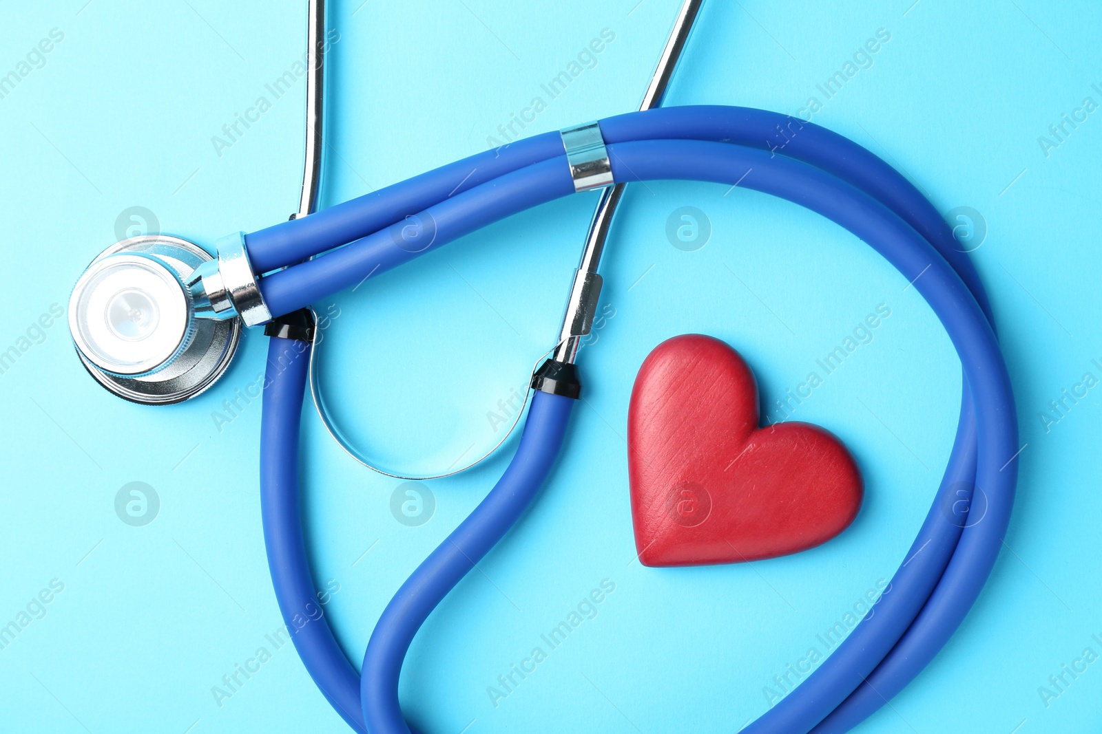 Photo of Cardiology. Stethoscope and red decorative heart on light blue background, flat lay