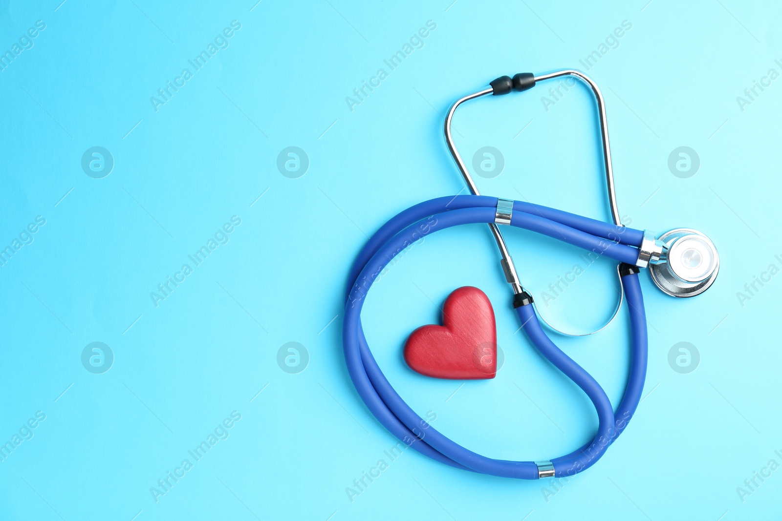 Photo of Cardiology. Stethoscope and red decorative heart on light blue background, flat lay. Space for text