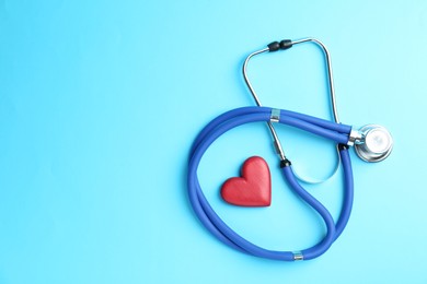 Photo of Cardiology. Stethoscope and red decorative heart on light blue background, flat lay. Space for text