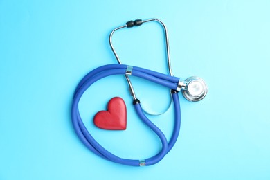 Photo of Cardiology. Stethoscope and red decorative heart on light blue background, flat lay