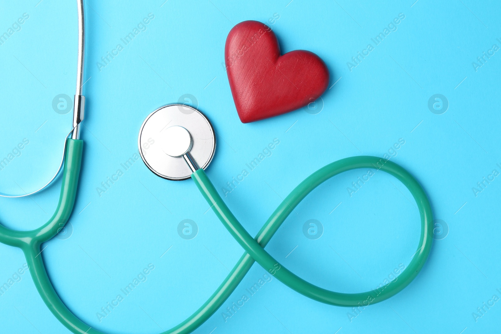 Photo of Cardiology. Stethoscope and red decorative heart on light blue background, flat lay