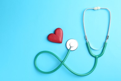 Photo of Cardiology. Stethoscope and red decorative heart on light blue background, flat lay. Space for text