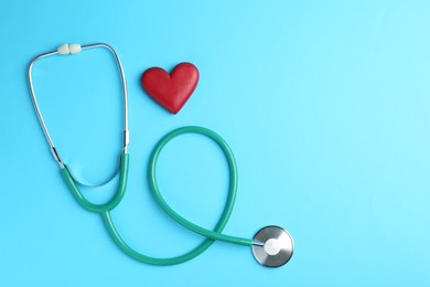 Photo of Cardiology. Stethoscope and red decorative heart on light blue background, flat lay. Space for text