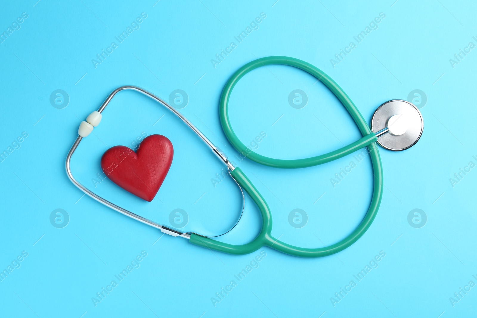 Photo of Cardiology. Stethoscope and red decorative heart on light blue background, flat lay