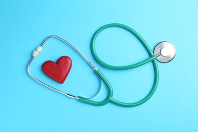 Photo of Cardiology. Stethoscope and red decorative heart on light blue background, flat lay