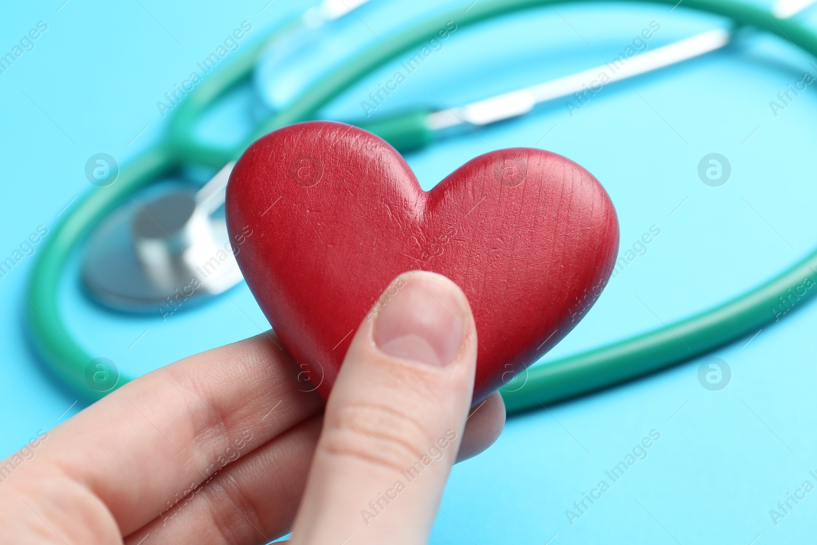 Photo of Cardiology. Woman with red decorative heart and stethoscope on light blue background, closeup