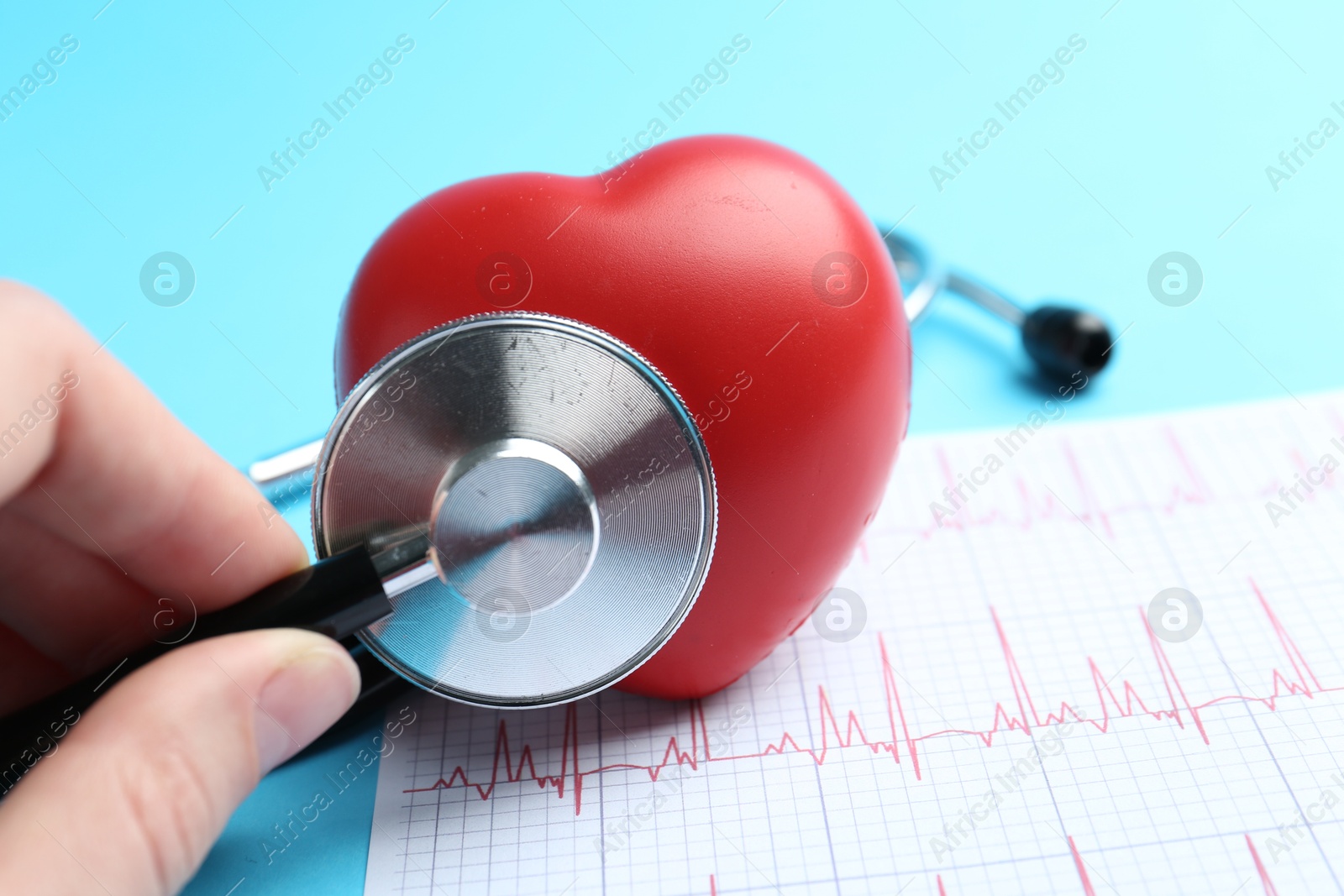 Photo of Cardiology. Woman with red decorative heart, cardiogram and stethoscope on light blue background, closeup