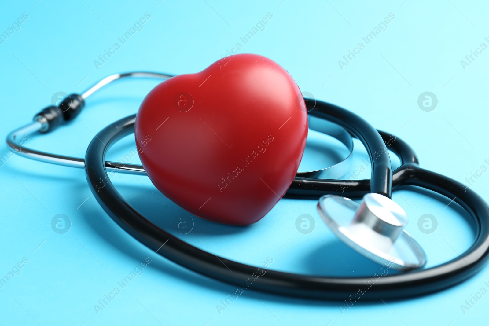 Photo of Cardiology. Stethoscope and red decorative heart on light blue background, closeup