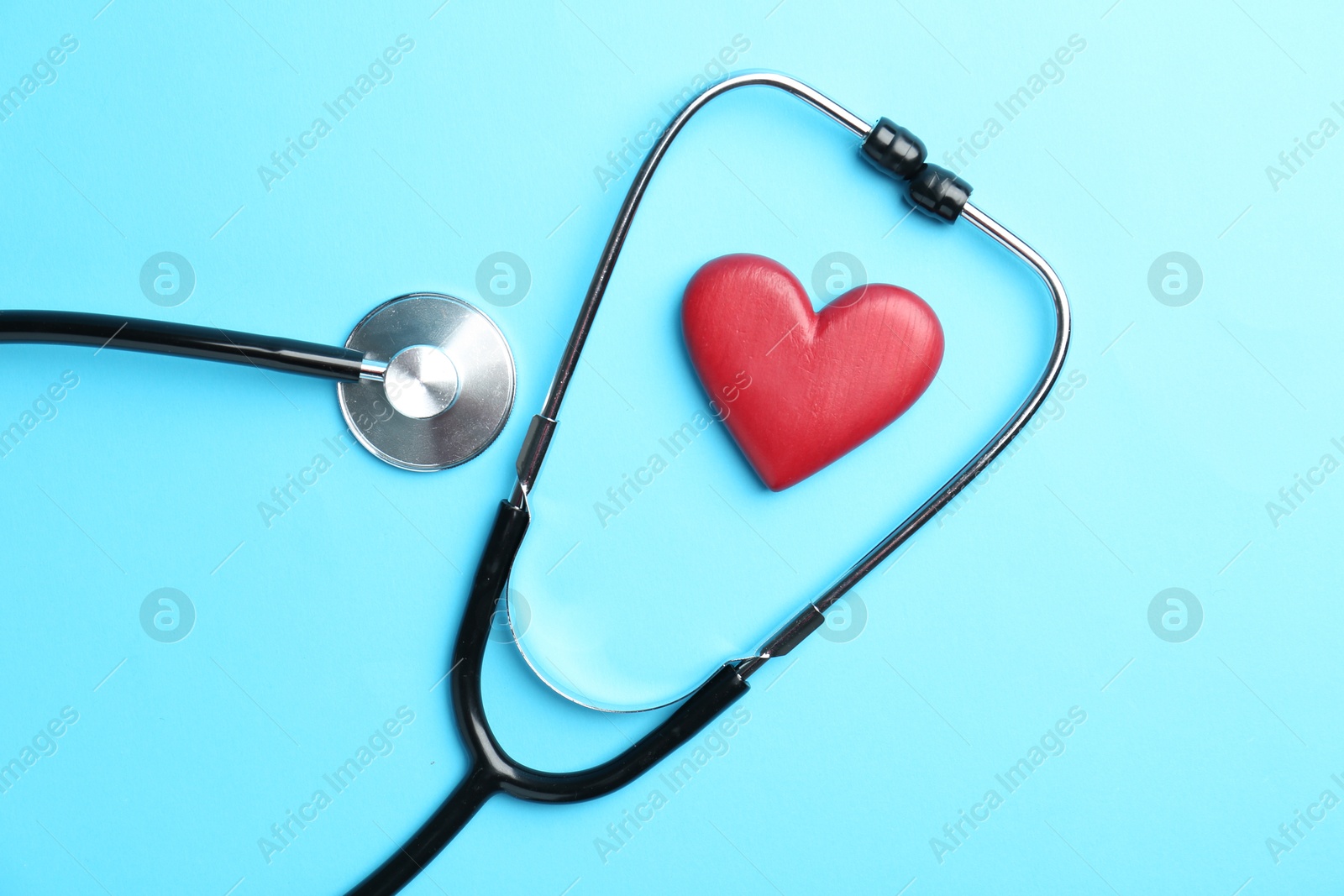 Photo of Cardiology. Stethoscope and red decorative heart on light blue background, flat lay