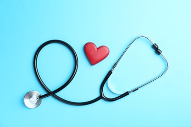 Photo of Cardiology. Stethoscope and red decorative heart on light blue background, flat lay