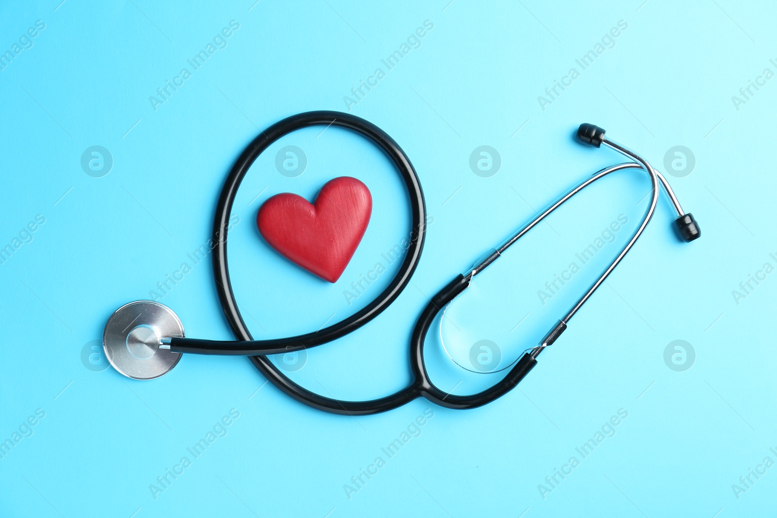 Photo of Cardiology. Stethoscope and red decorative heart on light blue background, flat lay