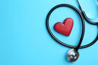 Photo of Cardiology. Stethoscope and red decorative heart on light blue background, flat lay. Space for text