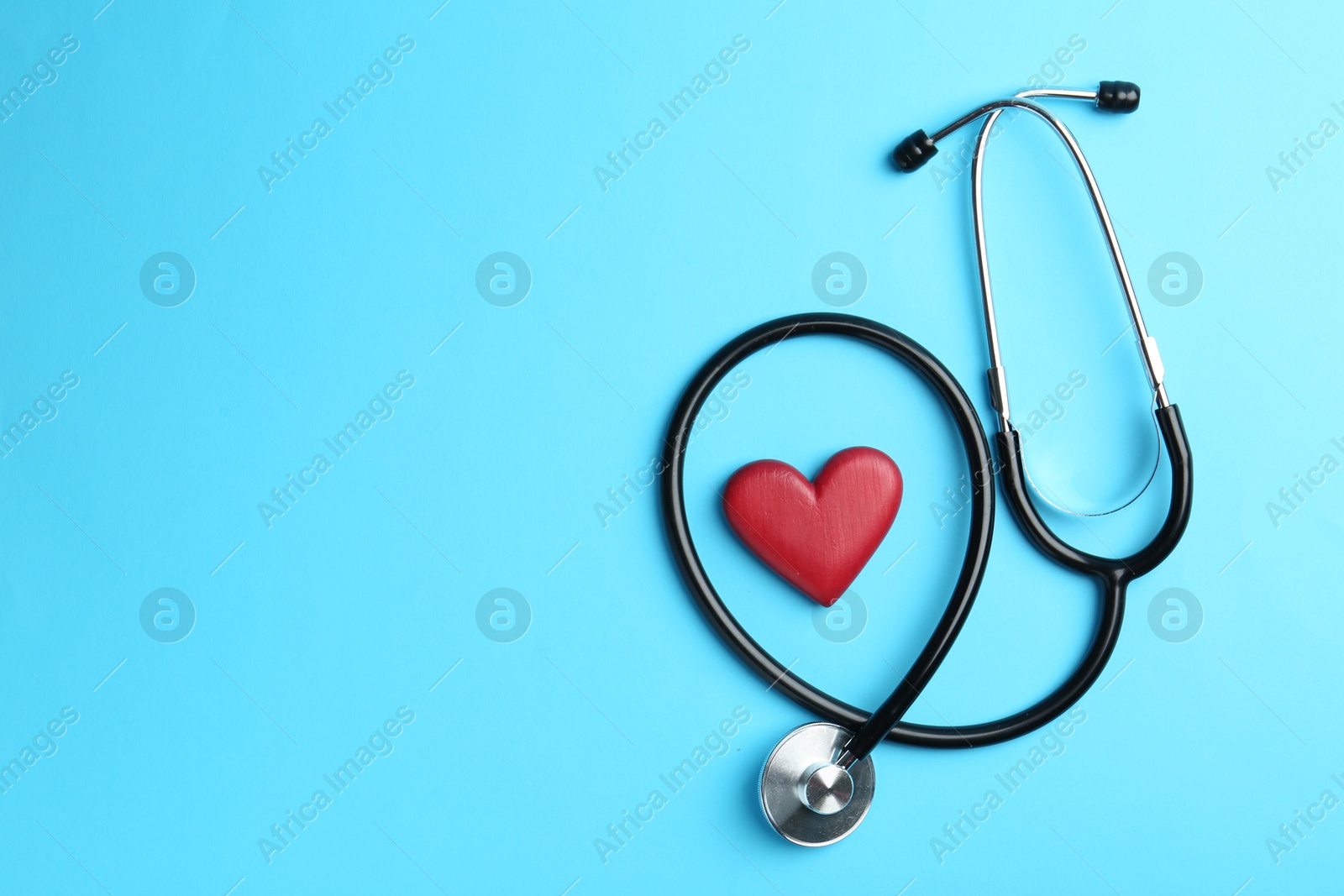 Photo of Cardiology. Stethoscope and red decorative heart on light blue background, flat lay. Space for text