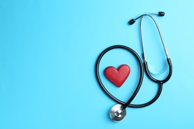 Photo of Cardiology. Stethoscope and red decorative heart on light blue background, flat lay. Space for text