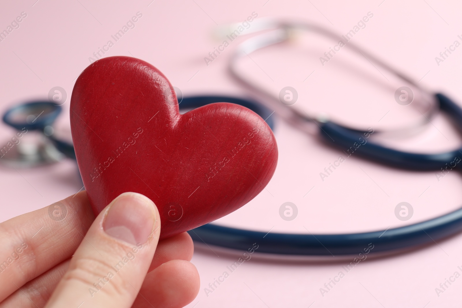 Photo of Cardiology. Woman with red decorative heart and stethoscope on pale pink background, closeup. Space for text