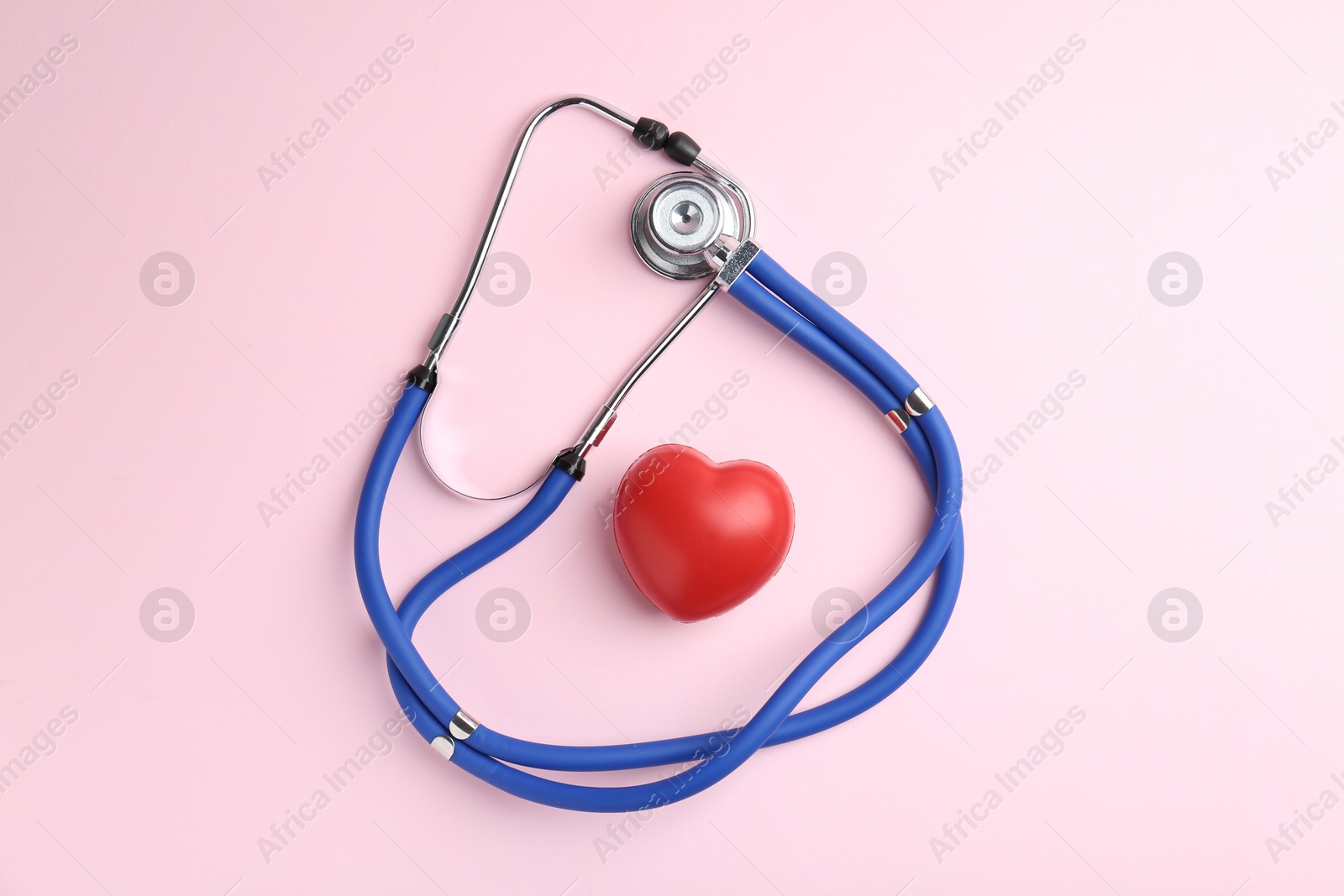 Photo of Cardiology. Stethoscope and red decorative heart on pale pink background, flat lay