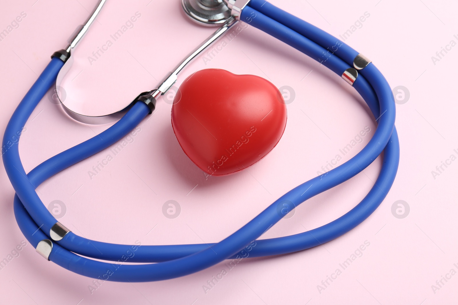 Photo of Cardiology. Stethoscope and red decorative heart on pale pink background, closeup