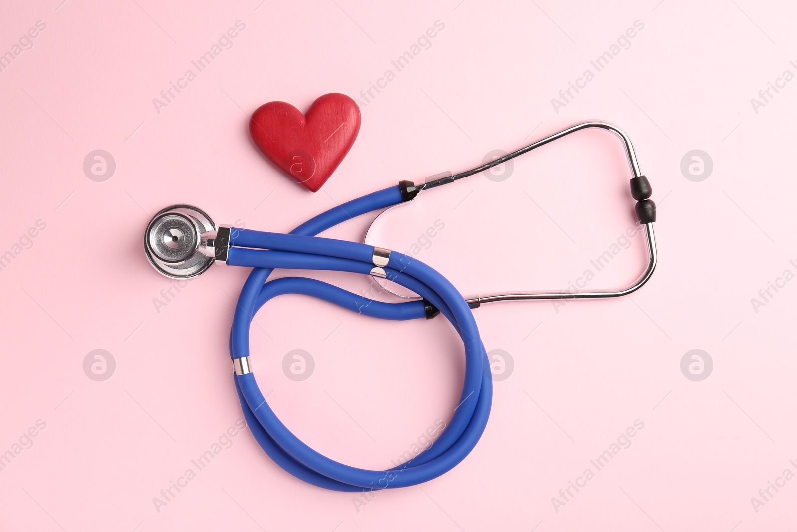 Photo of Cardiology. Stethoscope and red decorative heart on pale pink background, flat lay