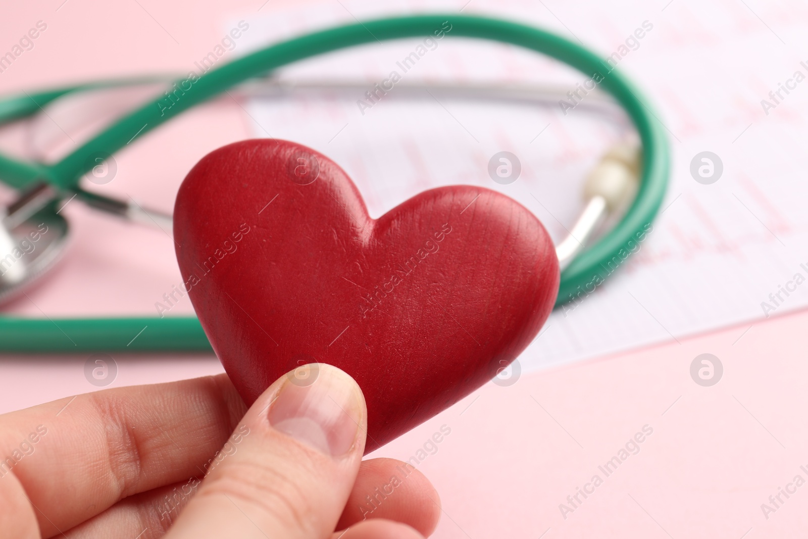 Photo of Cardiology. Woman with red decorative heart, cardiogram and stethoscope on pale pink background, closeup