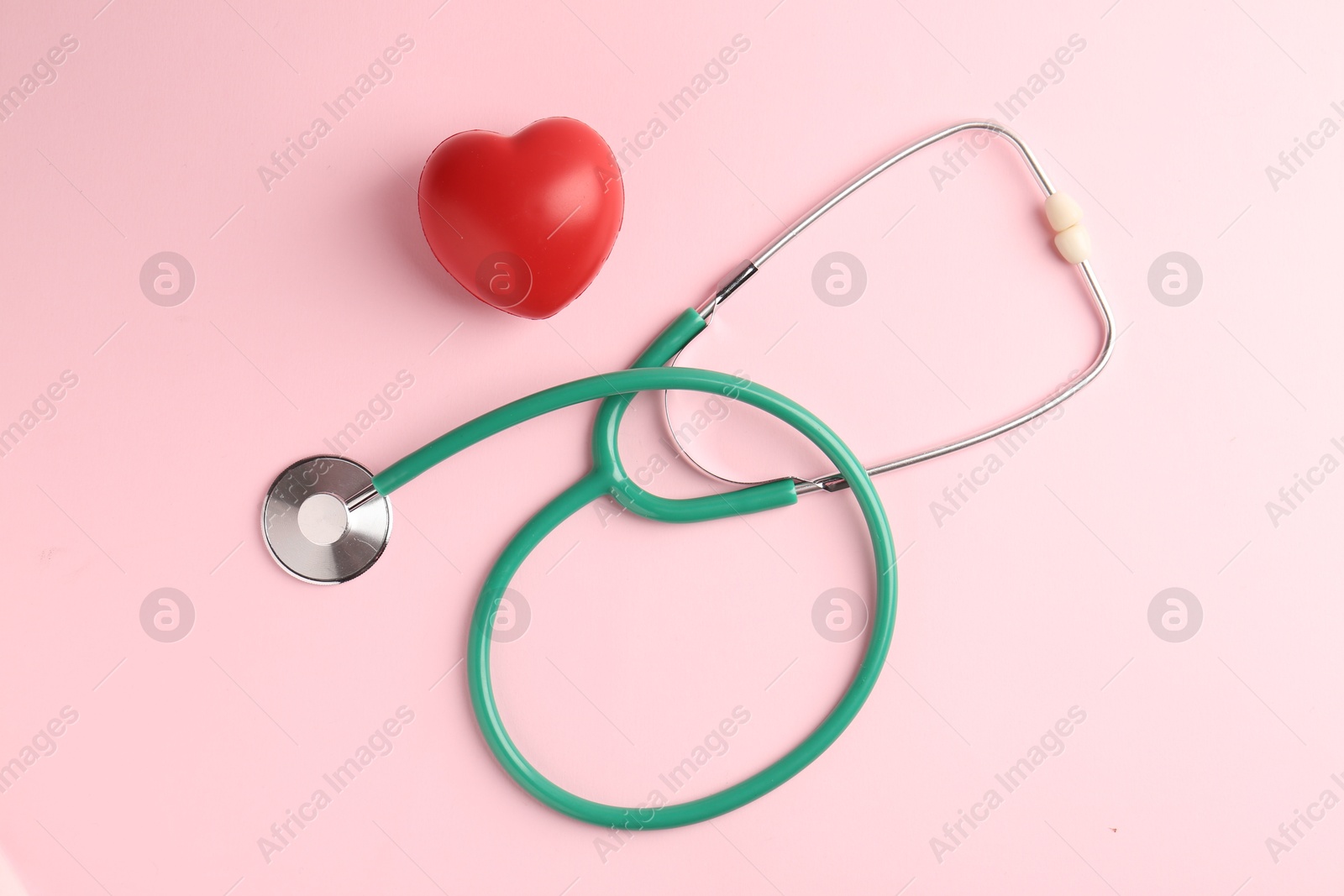 Photo of Cardiology. Stethoscope and red decorative heart on pale pink background, flat lay