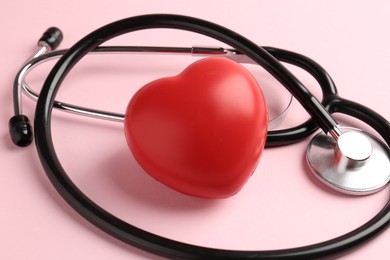 Photo of Cardiology. Stethoscope and red decorative heart on pale pink background, closeup