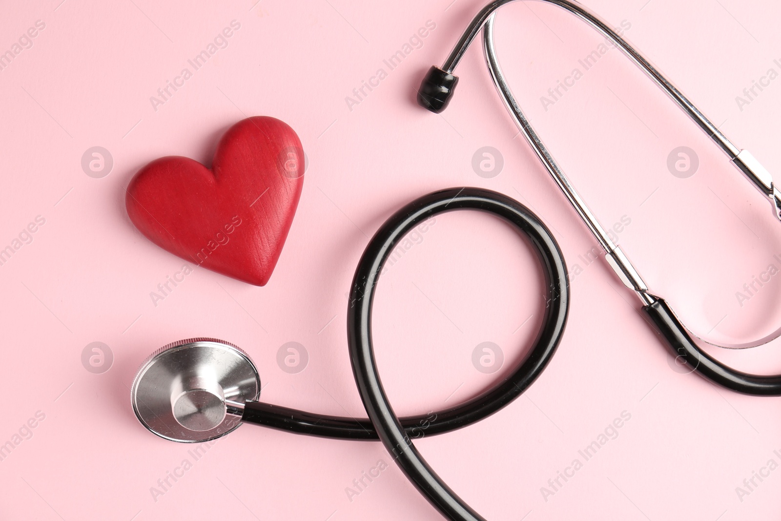 Photo of Cardiology. Stethoscope and red decorative heart on pale pink background, flat lay