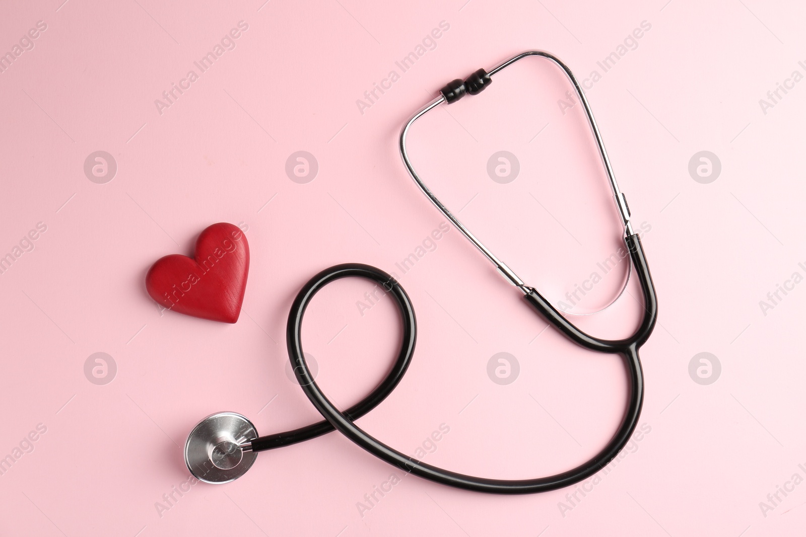 Photo of Cardiology. Stethoscope and red decorative heart on pale pink background, flat lay