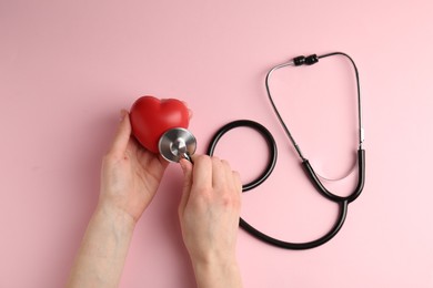 Photo of Cardiology. Woman with red decorative heart and stethoscope on pale pink background, top view