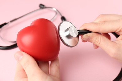 Photo of Cardiology. Woman with red decorative heart and stethoscope on pale pink background, closeup