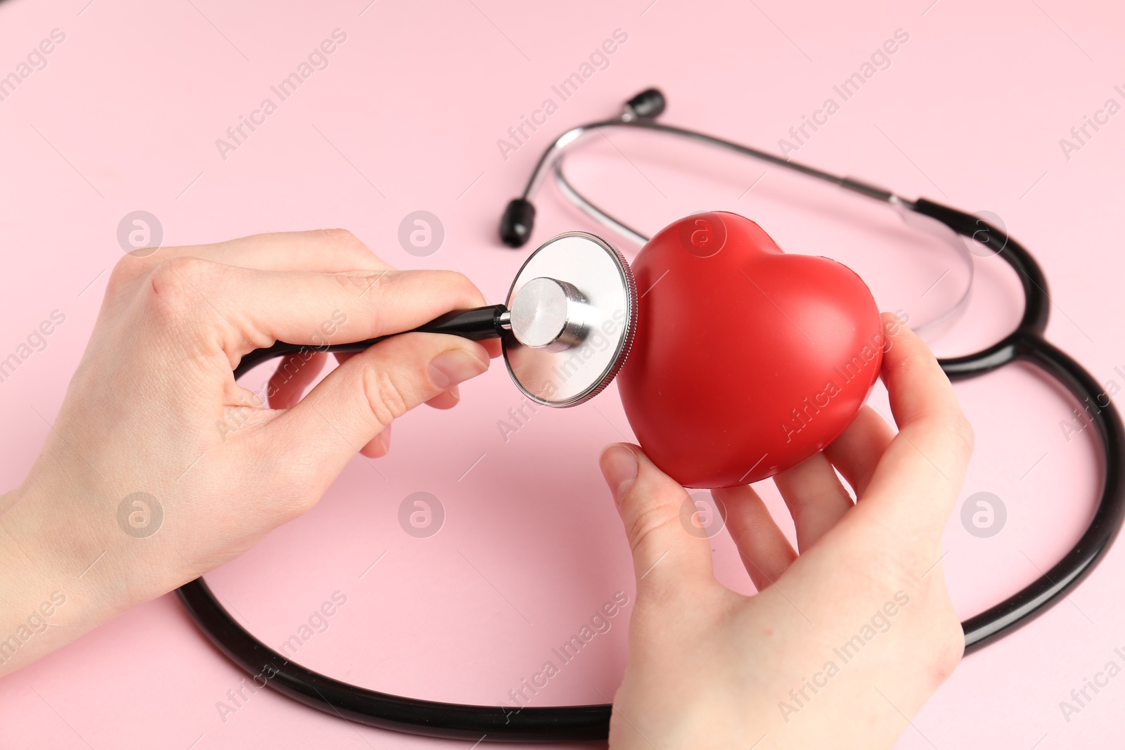 Photo of Cardiology. Woman with red decorative heart and stethoscope on pale pink background, closeup