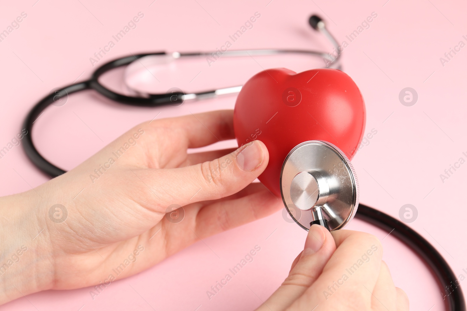 Photo of Cardiology. Woman with red decorative heart and stethoscope on pale pink background, closeup