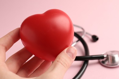 Photo of Cardiology. Woman with red decorative heart and stethoscope on pale pink background, closeup