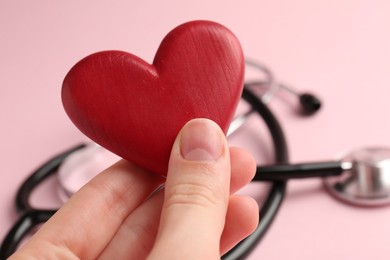 Photo of Cardiology. Woman with red decorative heart and stethoscope on pale pink background, closeup