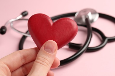 Photo of Cardiology. Woman with red decorative heart and stethoscope on pale pink background, closeup