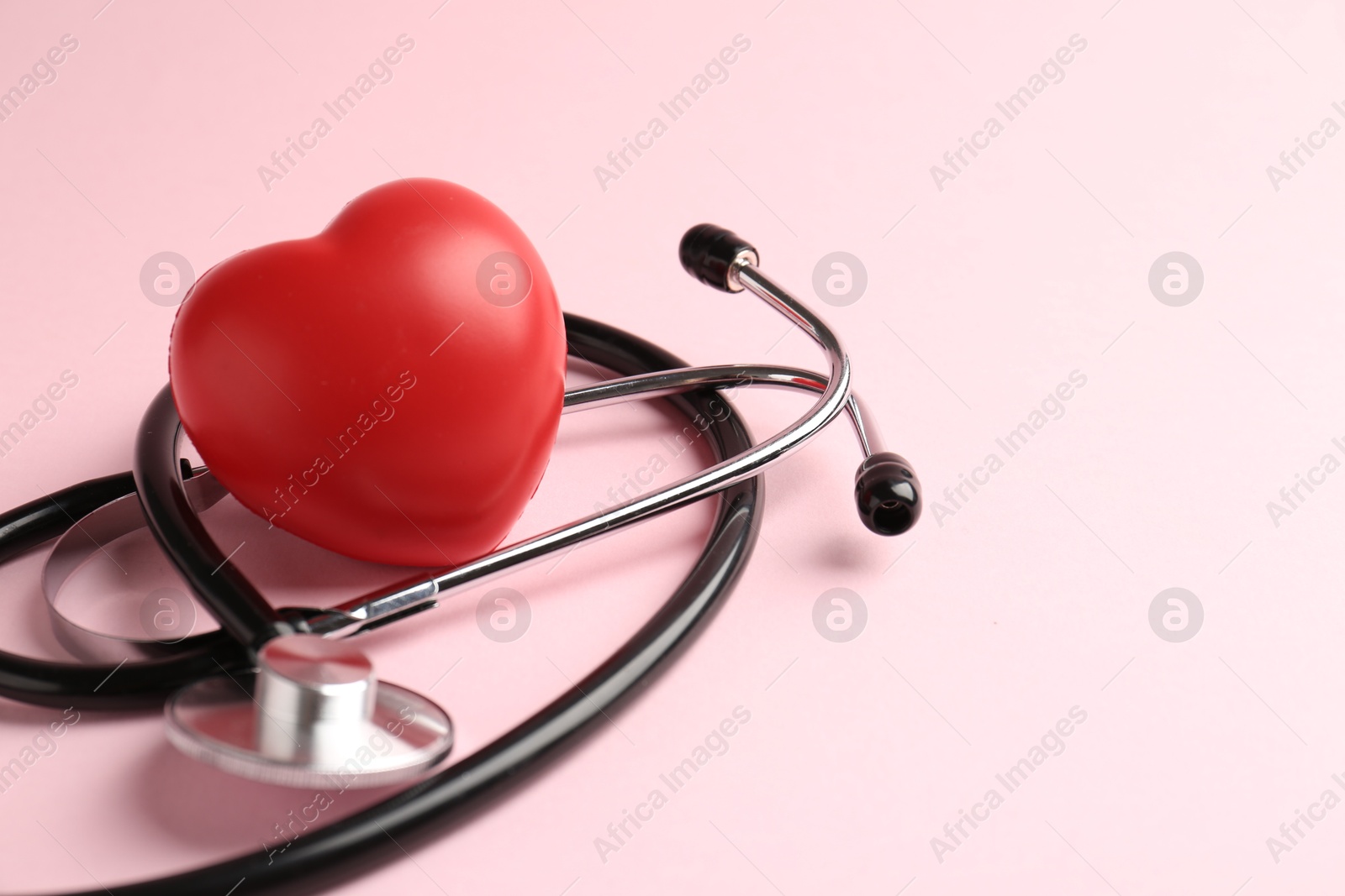 Photo of Cardiology. Stethoscope and red decorative heart on pale pink background, closeup. Space for text