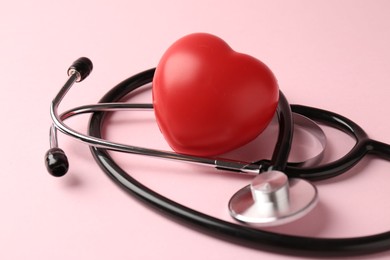 Photo of Cardiology. Stethoscope and red decorative heart on pale pink background, closeup