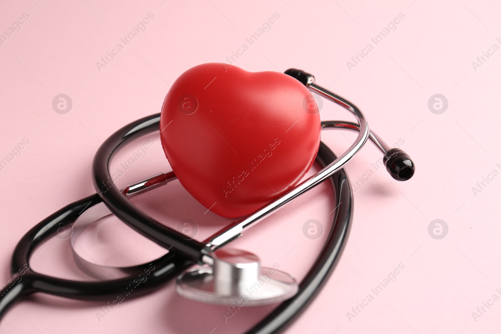 Photo of Cardiology. Stethoscope and red decorative heart on pale pink background, closeup