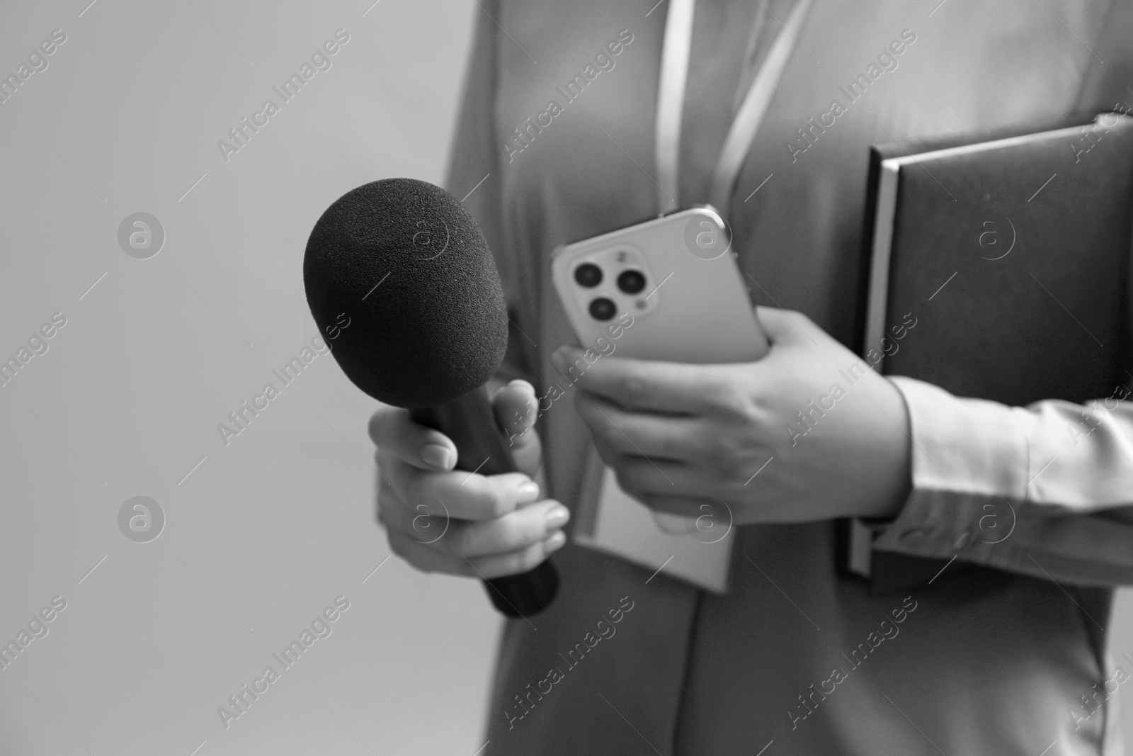 Image of Journalist with microphone, mobile phone and notebook taking interview, closeup. Toned in black-and-white