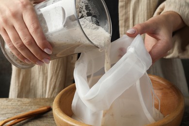 Photo of Making almond milk. Woman pouring nut mixture into cheesecloth at wooden table, closeup