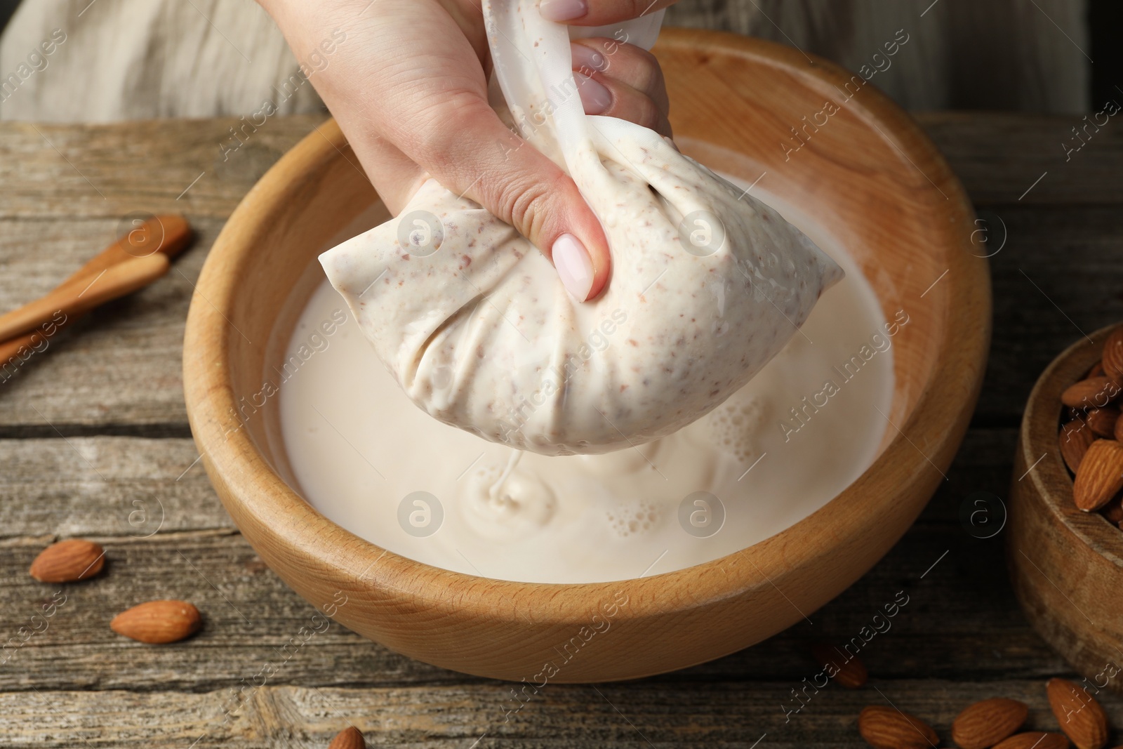 Photo of Woman making almond milk at wooden table, closeup