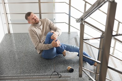 Photo of Man with injured knee on stairs in building after fall. Dangerous accident