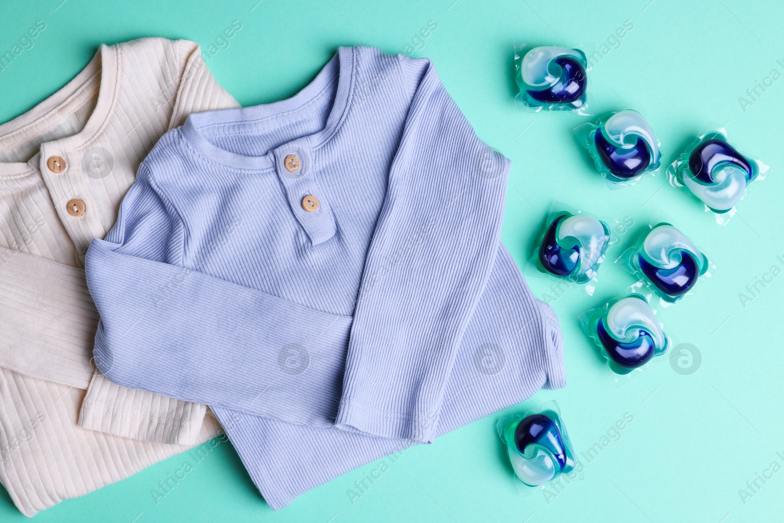 Photo of Laundry detergent capsules and clothes on turquoise background, flat lay