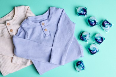 Photo of Laundry detergent capsules and clothes on turquoise background, flat lay