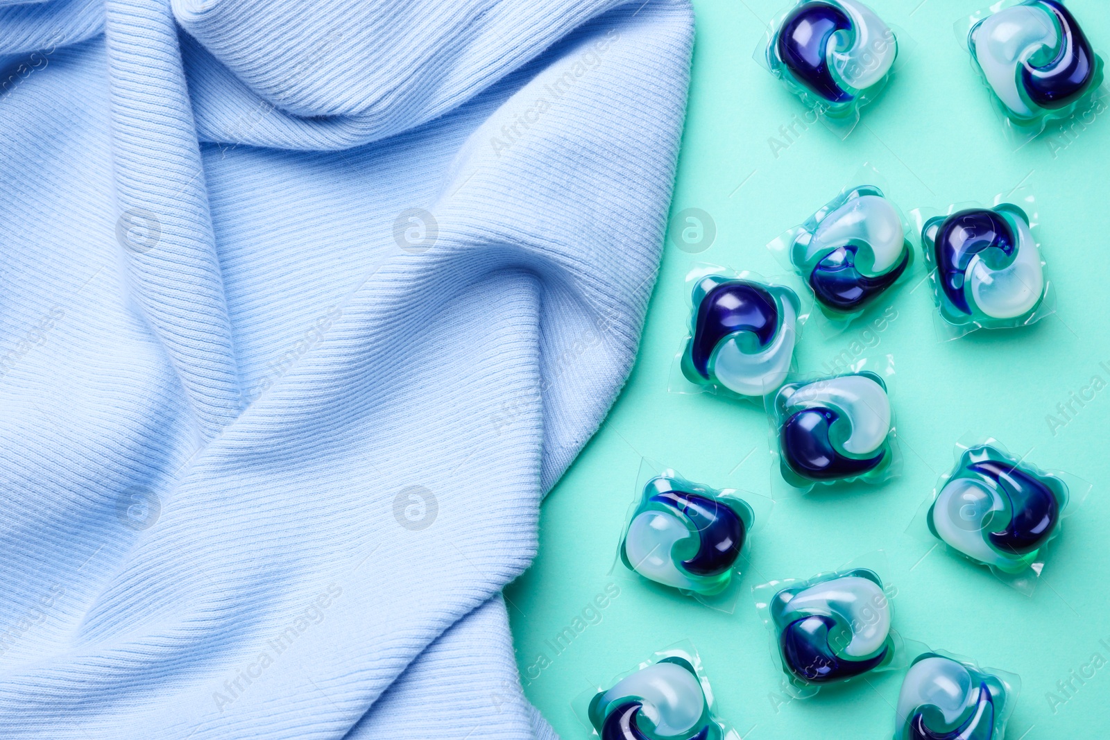 Photo of Laundry detergent capsules and clothes on turquoise background, flat lay