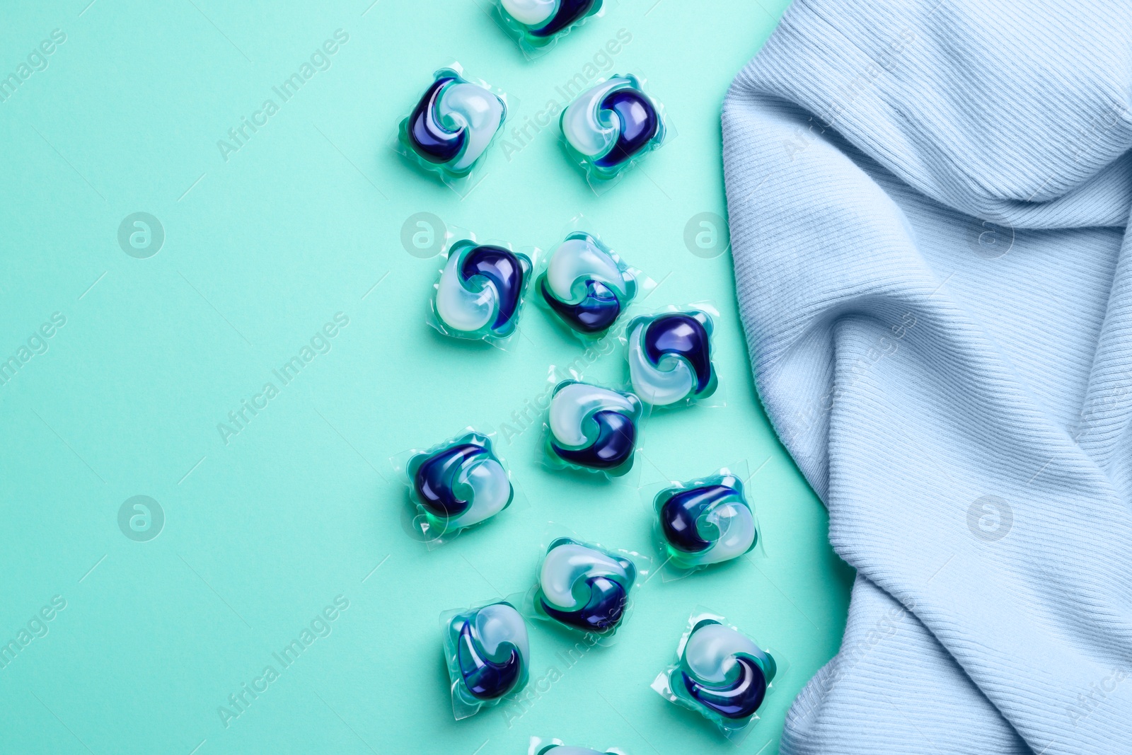 Photo of Laundry detergent capsules and clothes on turquoise background, flat lay