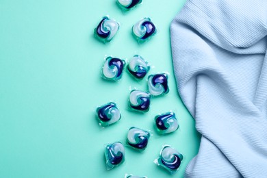 Photo of Laundry detergent capsules and clothes on turquoise background, flat lay