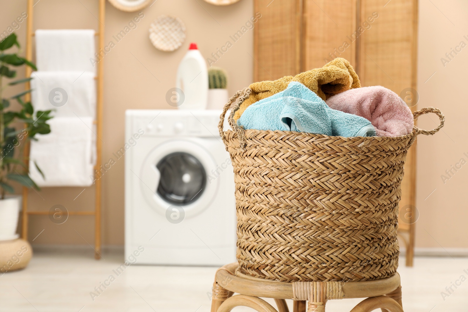 Photo of Wicker basket full of laundry on chair in bathroom