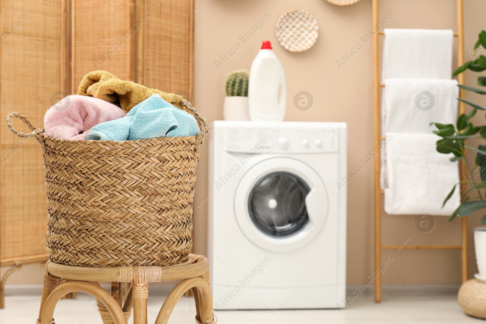 Photo of Wicker basket full of laundry on chair in bathroom