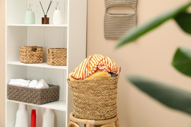 Photo of Wicker basket full of laundry on chair in bathroom